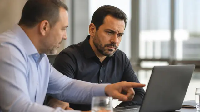 CFO analisando com atenção uma tela de laptop ao lado de um colega em reunião